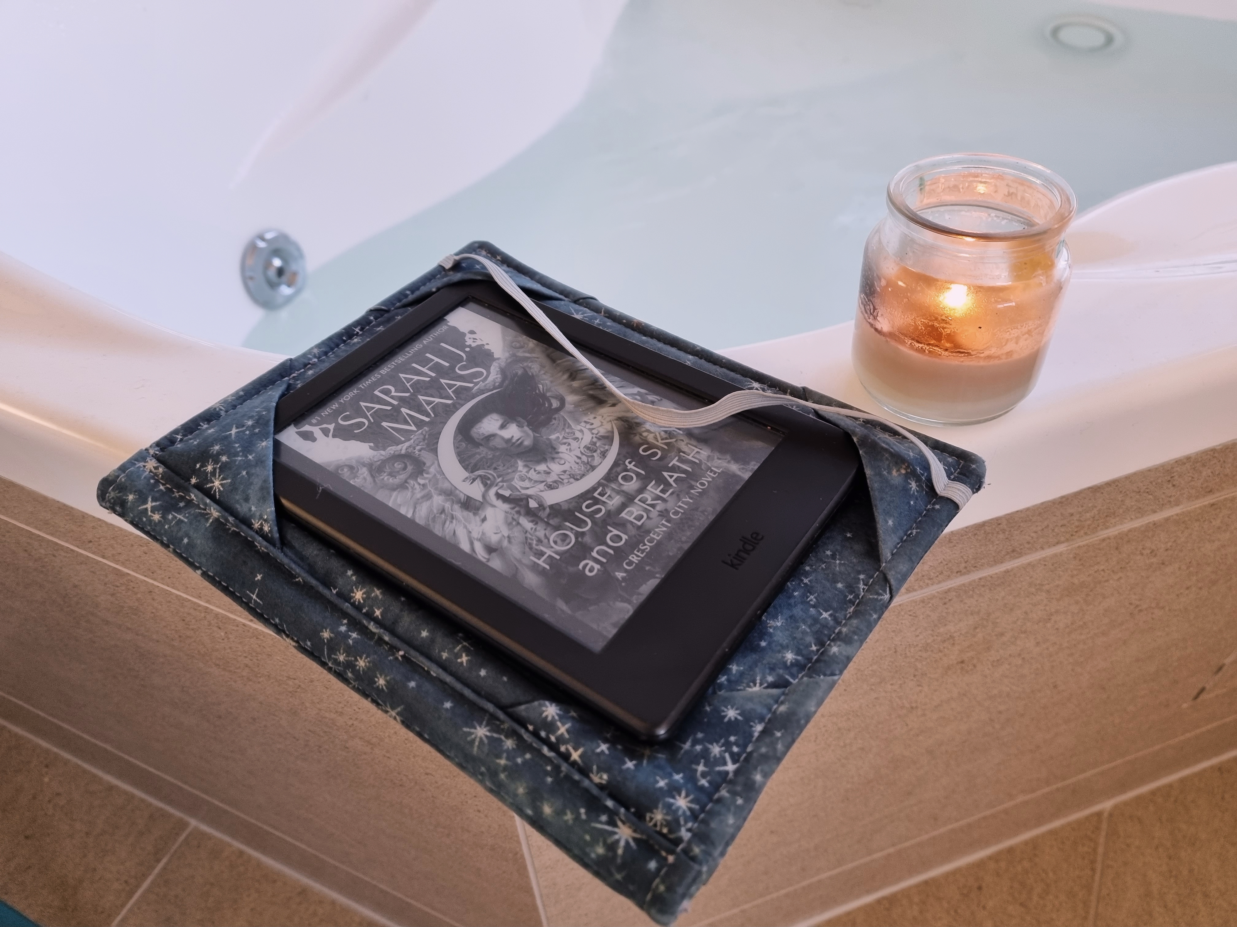 Kindle showing House of Sky and Breath and a lit candle on the edge of a bath